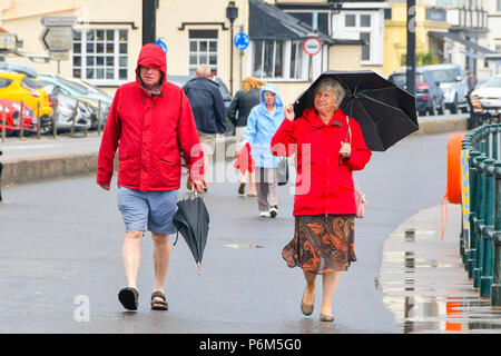 Honiton, Devon, Großbritannien. 1. Juli 2018. UK Wetter. Besucher in den Badeort Sidmouth Devon mit Sonnenschirmen, wie die Stadt fängt den Rand eines vorbeifahrenden heftiger Regenschauer. Foto: Graham Jagd-/Alamy leben Nachrichten Stockfoto