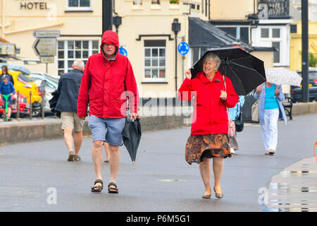 Honiton, Devon, Großbritannien. 1. Juli 2018. UK Wetter. Besucher in den Badeort Sidmouth Devon mit Sonnenschirmen, wie die Stadt fängt den Rand eines vorbeifahrenden heftiger Regenschauer. Foto: Graham Jagd-/Alamy leben Nachrichten Stockfoto