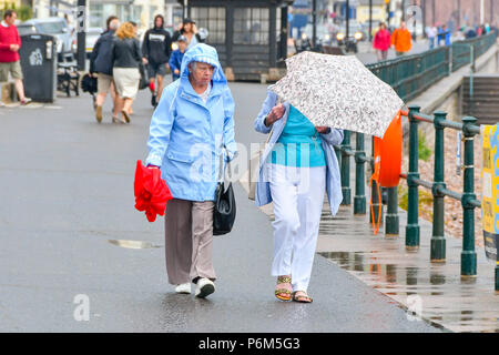 Honiton, Devon, Großbritannien. 1. Juli 2018. UK Wetter. Besucher in den Badeort Sidmouth Devon mit Sonnenschirmen, wie die Stadt fängt den Rand eines vorbeifahrenden heftiger Regenschauer. Foto: Graham Jagd-/Alamy leben Nachrichten Stockfoto