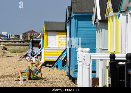 Weibliche Sonnenanbeter durch mehrfarbige bunten Holzhütten am Southend On Sea, Essex, Großbritannien Stockfoto