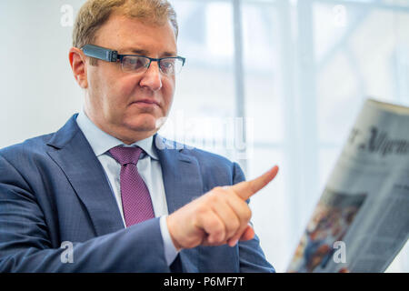 München, Deutschland. 29 Mai, 2018. Ziv Aviram, Manager der Elektronikhersteller Orcam, trug einen Prototyp der Miniaturkamera bin yEye', während eine Zeitung Artikel zu ihm gelesen wird. Die finger Gerät bin yEye" vereint Kamera, Lautsprecher und künstliche Intelligenz und liest Texte oder Banknoten erkannt durch Handzeichen. Credit: Lino Mirgeler/dpa/Alamy leben Nachrichten Stockfoto
