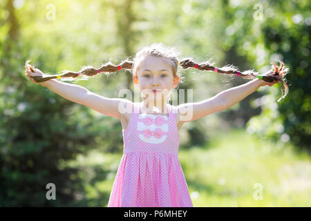 Ein Mädchen im roten Kleid hält Ihr Haar geflochten in Pigtails mit ihren Händen. Stockfoto