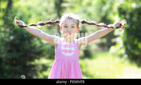 Ein Mädchen im roten Kleid hält Ihr Haar geflochten in Pigtails mit ihren Händen. Stockfoto