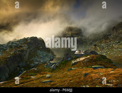 Schönen alpinen Berglandschaft mit dramatischen Himmel und alte steinerne Hütte. Berghütte in der Nähe von kleinen alpinen See. Rila-gebirge, Bulgarien. Stockfoto