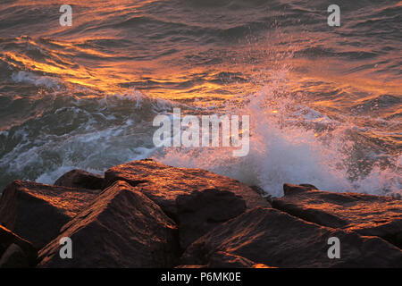 Warnemünde, Wellen im Abendlicht auf Felsen brechen Stockfoto