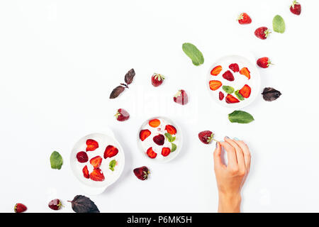 Woman's Hand, denn frische Erdbeere unter den Schalen von Speiseeis auf weißem Hintergrund, Ansicht von oben. Flach Anordnung der Sommer kalte Desserts eingerichtet wi Stockfoto