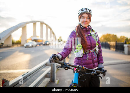 Foto von sportliche Frau in Helm auf dem Fahrrad auf Brücke in der Stadt Stockfoto