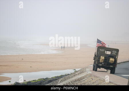 Vierville-sur-Mer, Frankreich. Ein Willys Jeep fliegen die US-Flagge sitzt auf der Ufermauer mit Blick auf Omaha Beach, als entfernte Paar Spaziergang entlang der Waters Edge am Jahrestag des D-Day Stockfoto