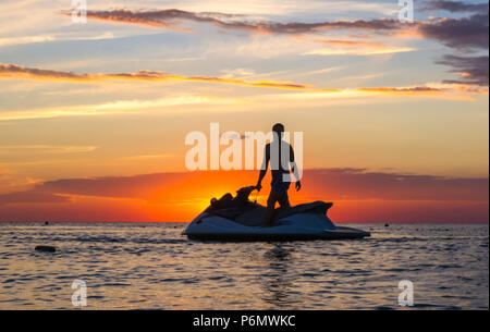 Silhouette eines Mannes auf einem Jet-ski in der Sonne auf dem Meer Sonnenuntergang im Sommer Abend Stockfoto