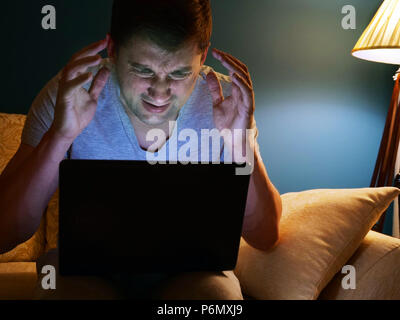 Erschrocken oder wütenden Mann mit Laptop auf einem Sofa. Am Abend Zeit. Stockfoto
