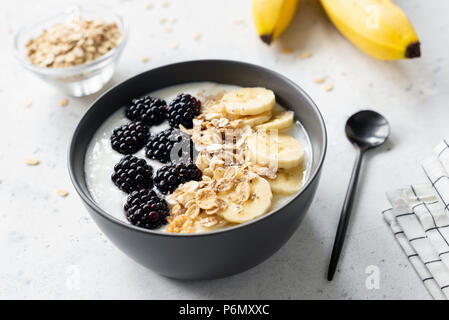 Frühstück smoothie Schüssel mit Bananen, Müsli und Blackberry auf grauem Beton Hintergrund, Detailansicht, selektiver Fokus Stockfoto