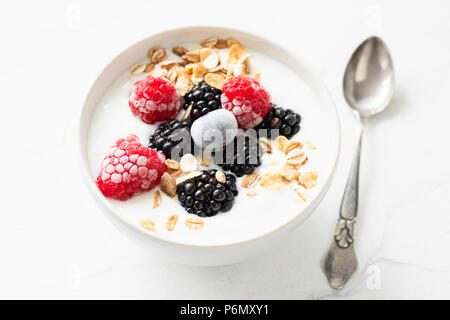 Joghurt mit Beeren und Haferflocken in eine Schüssel geben. Detailansicht. Gesunde Ernährung, gesunde Lebensweise Konzept Stockfoto