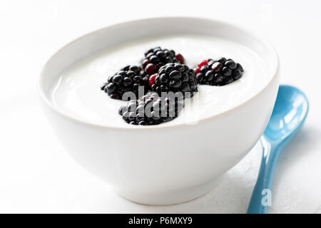 Joghurt mit Brombeeren in eine Schüssel geben. Auf weiß isoliert. Gesunde Ernährung Konzept Stockfoto