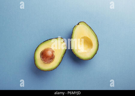 Zwei Hälften von Avocado mit Saatgut auf blauem Hintergrund. Ansicht von oben, minimale gestaltete Komposition. Stockfoto