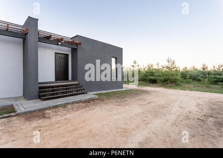 Seitenansicht eines offenen Veranda vor einem modernen Forest Cottage. Kiefer junge Wald unter den Sonnenuntergang strahlen im Hintergrund. Stockfoto