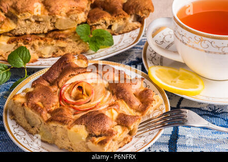 Leckeren warmen Apfelkuchen auf Platte mit Deckel von Tee. Ein Stück des Kuchens mit in Scheiben geschnittenen roten Apfel in der Mitte. Berühmte Tarte mit verschiedenen Arten von Rezepten. Stockfoto