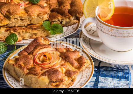 Leckeren warmen Apfelkuchen auf Platte mit Deckel von Tee. Ein Stück des Kuchens mit in Scheiben geschnittenen roten Apfel in der Mitte. Berühmte Tarte mit verschiedenen Arten von Rezepten. Stockfoto