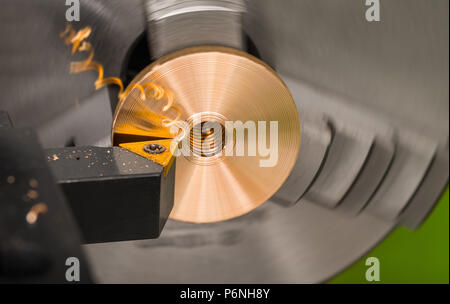 Nahaufnahme eines Werkzeug bit beim Drehen auf einer Drehbank. Bronze Produkt in einem rotierenden Chuck der Maschine im Hintergrund gespannt. Späne und Spiegelung verdreht. Stockfoto