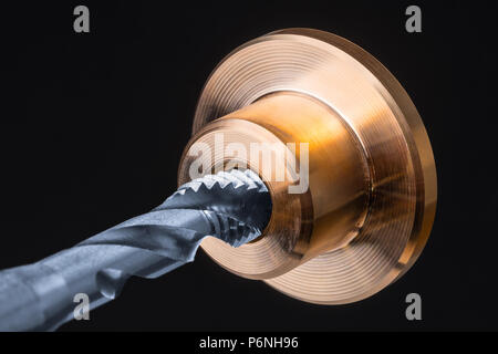 Detail der Spiralnut in goldene Metallteil tippen. Künstlerische Nahaufnahme einer silber-blau Stahl Schneidwerkzeug für Threading und Bronze Werkstück. Tippen. Stockfoto