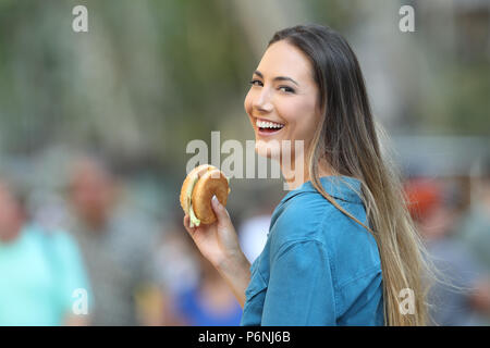 Happy woman holding einen Burger in suchen Sie auf der Straße Stockfoto