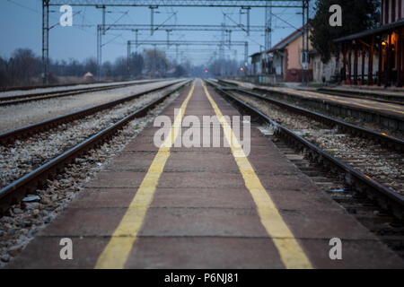 Alter Bahnhof Plattform mit den markanten gelben Sicherheit Linien auf einem fast verlassene elektrifizierte Bahnstrecke bei Sonnenuntergang Bild eines concreite Stockfoto