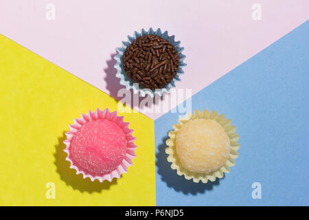 Brasilianische Spezialitäten: Brigadeiro, Beijinho und Bicho de Pe. Kindergeburtstag. Flache Ausführung von candy Kugel auf farbigen Hintergrund. Stockfoto