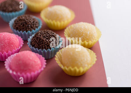 Brasilianische Spezialitäten: Brigadeiro, Beijinho und Bicho de Pe. Kindergeburtstag. Candy Kugeln in einer geraden Linie. Bunter Hintergrund. Stockfoto