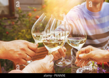 Familie unterschiedlichen Alters Menschen fröhlich feiern im Freien mit Gläsern Weißwein, verkünden Toast Menschen mit Abendessen in einem Haus Garten im Sommer Sonnenlicht. Stockfoto