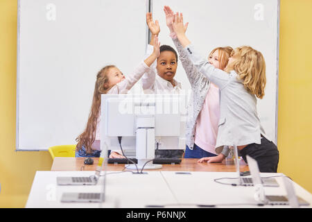 Gruppe Kinder im Computer unterricht gibt sich eine hohe fünf als Unterstützung Stockfoto