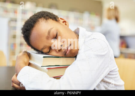 Schlafenden Jungen als Schüler in der Bibliothek mit einem großen Stapel Bücher Stockfoto