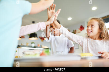 Kinder feiern Teamgeist mit hohen Fünf in der Grundschule Kantine Stockfoto