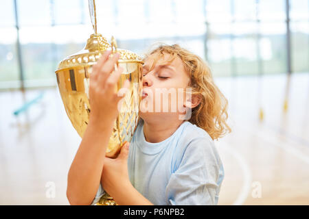 Blonde junge küsst ein Sieger cup nach einem sportlichen Wettbewerb Stockfoto