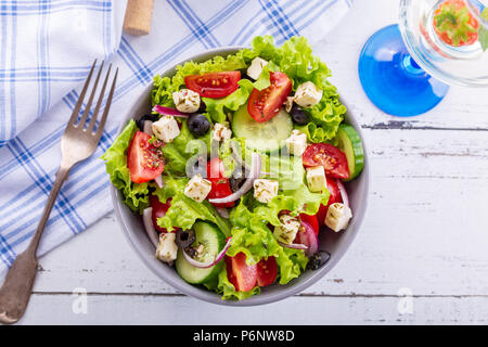 Griechischer Salat frisch serviert in der Schüssel mit einem Glas Weisswein. Stockfoto