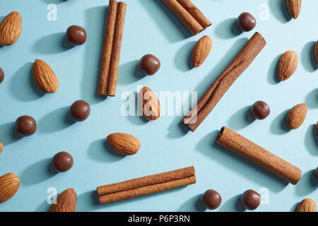 Eine Reihe von Schokolade Kugeln, Mandeln und Zimt Sticks in Form eines Musters mit Reflexion der Schatten auf einem blauen Hintergrund. Flach Stockfoto