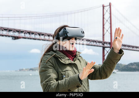 Junge schöne Mädchen mit Virtual reality Brillen. 25 April Brücke in Lissabon im Hintergrund. Das Konzept der modernen Technologien und deren Einsatz im täglichen Leben Stockfoto