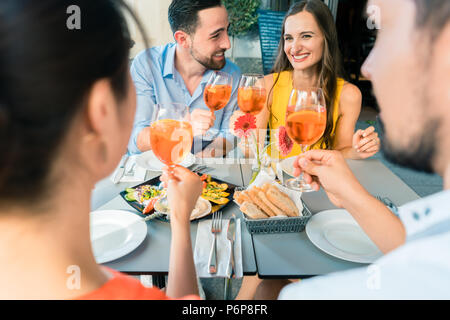 Zwei glückliche junge Paare toasten beim zusammen im Restaurant sitzen Stockfoto