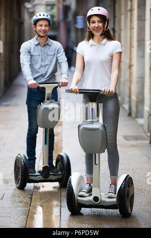 Junge freundliche Paar fahren Segways und lächelnd. Fokus auf Frauen Stockfoto