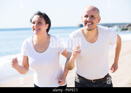 Gerne aktiv Reifes Paar im weißen T-Shirts jogging zusammen am Meer Stockfoto