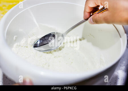 Die Hand das Mehl von Löffel in die weiße Schüssel Stockfoto