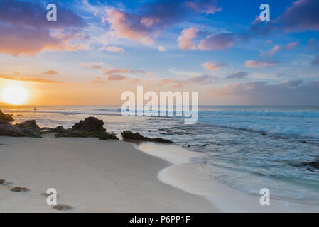 Rubrik Surfer bei Sonnenuntergang am Sunset Beach auf der North Shore von Oahu, Hawaii mit Palmen und Surf rollen in am Sandstrand Stockfoto