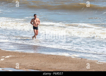 Skegness, Großbritannien, 2. Juli 2018. Ein Mann Jogging am Strand verwendet die ankommenden Wellen zu halten sich cool, wie die anhaltende warme Wetter Temperaturen in Großbritannien hält auf einem hohen. Credit: Steven Booth/Alamy Leben Nachrichten. Stockfoto