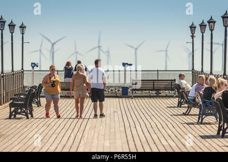 Skegness, Großbritannien. 2. Juli 2018. Touristen genießen die warme Wetter auf Skegness Pier und Anzeigen der Offshore-Windparks durch die Hitze Dunst an der Ostküste in Richtung der normalerweise kalten Nordsee. Credit: Steven Booth/Alamy Leben Nachrichten. Stockfoto