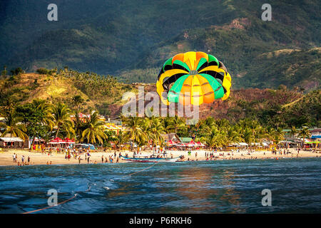 Parasailing über Weißen Strand mit Bergen im Hintergrund bei Puerto Galera, Oriental Mindoro, Philippinen. Stockfoto