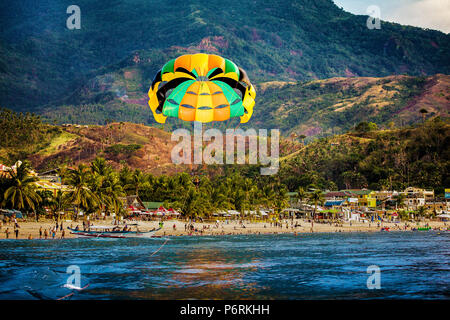 Gleitschirmfliegen in der Nähe von Wasser über den weißen Strand von Puerto Galera, Oriental Mindoro, Philippinen. Stockfoto