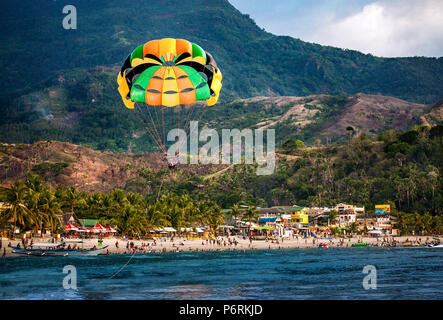 Parasailing über Weißen Strand gefüllt mit Hunderten von Menschen im Urlaub in Puerto Galera, Oriental Mindoro, Philippinen. Stockfoto