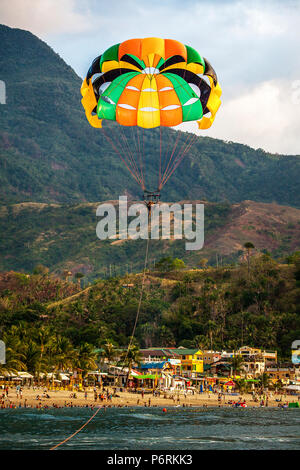 Parasailing über Weißen Strand mit Urlauber in Puerto Galera, Oriental Mindoro, Philippinen. Stockfoto