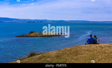 Romantisches Paar sitzen auf einem Hügel und bietet einen Blick auf die St. Cuthbert Insel, von der die heilige Insel von Lindisfarne, Northumberland, England genießen Stockfoto