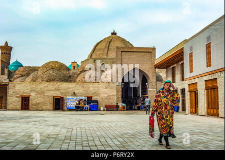 Eine Frau geht in einem offenen Raum mit Bazar Taki-Zargaron im Hintergrund, Buchara, Usbekistan Stockfoto