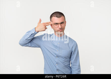 Müde oder gelangweilt Hispanic guy Holding gun Geste in der Nähe von Tempeln und Grimassen während über grauer Hintergrund stehen. Stockfoto