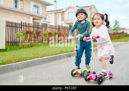 Süße Kinder reiten Roller Stockfoto